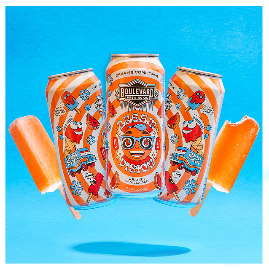 Three cans of Boulevard Brewing Co. “Dream Vision” orange vanilla ale against a bright blue background. The cans are decorated with whimsical images including ice cream and popsicles. Two orange popsicles with bites taken out are positioned beside the cans.