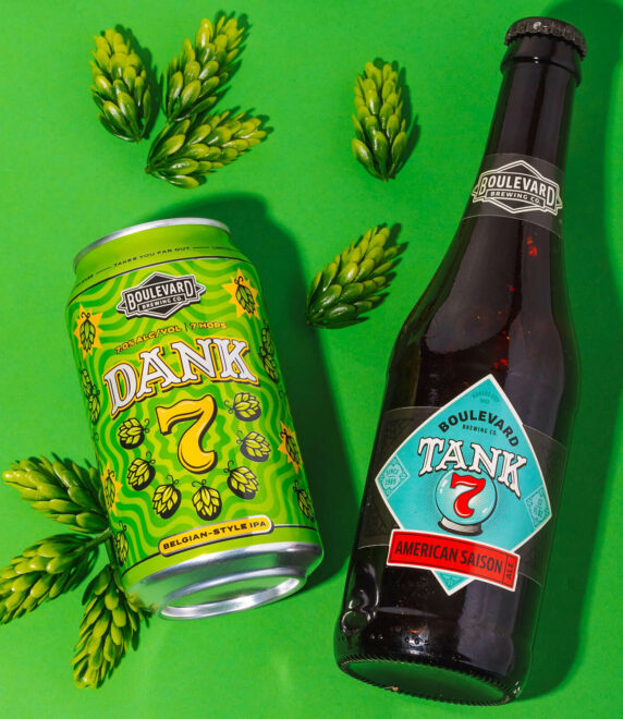 An image of two Boulevard Brewing Co. beers on a lime green background, surrounded by hop cones. On the left is a can of "Dank 7" Belgian-Style IPA in green and yellow colors, and on the right is a bottle of "Tank 7" American Saison with a blue and red label.