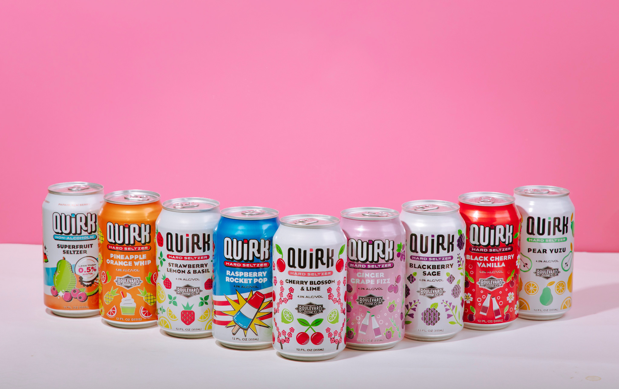 A row of Quirk Hard Seltzer cans lined up against a pink background. The flavors displayed from left to right include Superberry, Pineapple Orange Whip, Strawberry Lemon Basil, Raspberry Rocket Pop, Cherry Blossom & Lime, Blackberry Sage, Blueberry Lemon & Lavender, Ginger & Hops, Black Cherry & Vanilla, and Pear Yuzu. Each can boasts vibrant designs reflecting its unique flavor