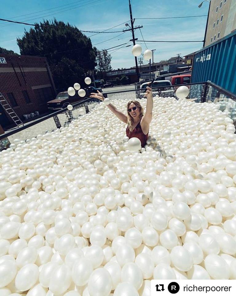 A person joyfully throwing white balls into the air, surrounded by a sea of similar balls in an outdoor urban setting.