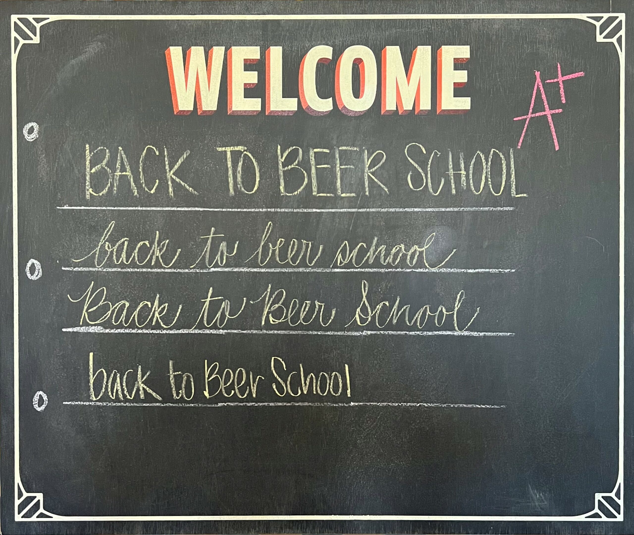 A blackboard with "WELCOME" in large, red letters at the top and a red "A+" next to it. Below, in different styles of handwriting, are the words "back to beer school" written four times with lines separating each version. The board has chalkboard borders.