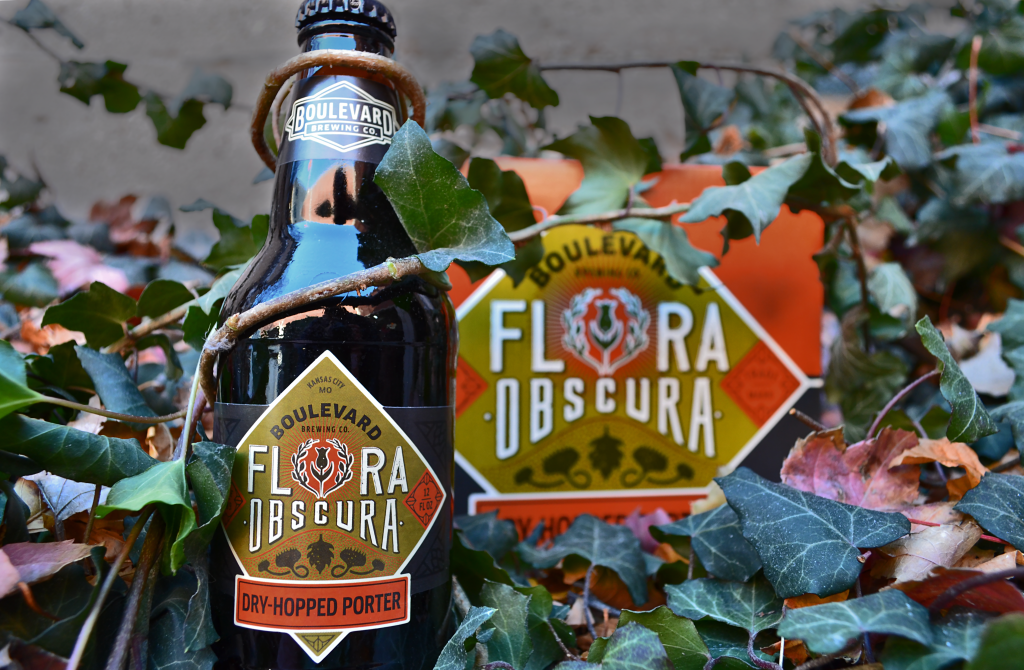 A bottle of Boulevard Brewing Co.'s Flora Obscura Dry-Hopped Porter is surrounded by autumn leaves. The bottle labels feature a decorative design with a hexagonal logo. The colors are rich and earthy.