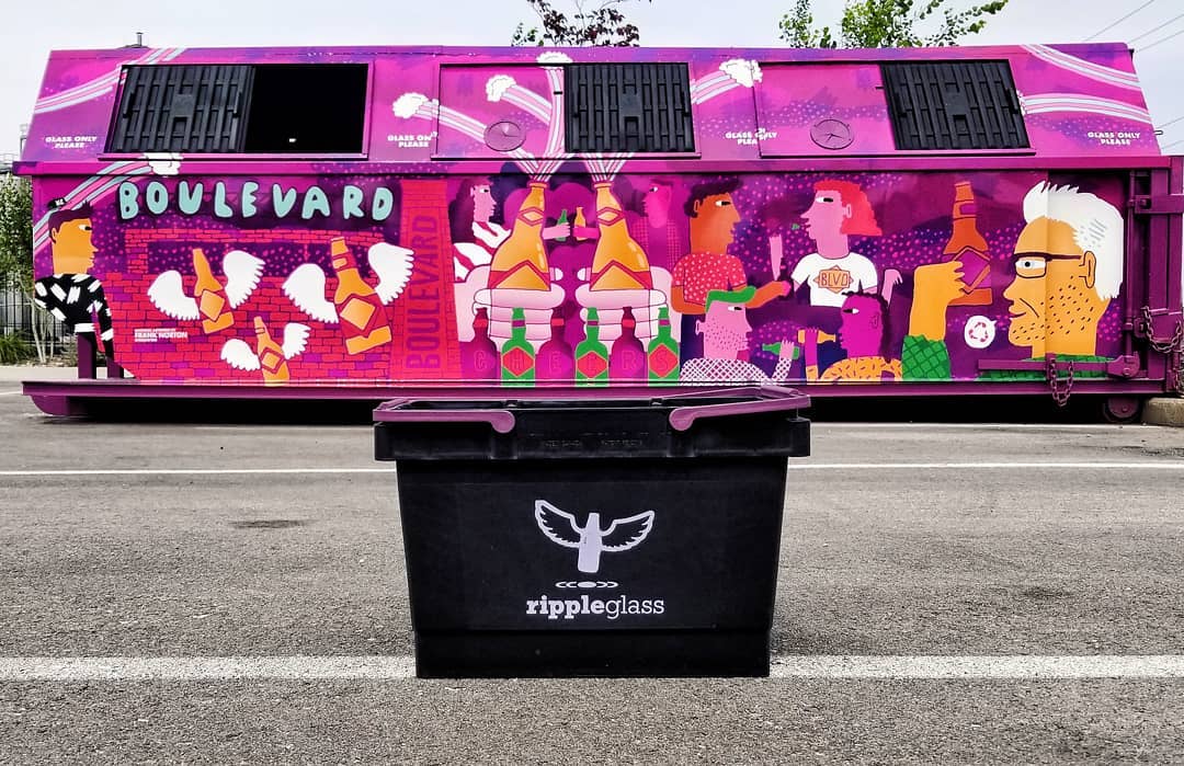 A black Ripple Glass recycling bin with a stylized winged logo sits in front of a large, vibrant mural about recycling. The mural features colorful illustrations of people, birds, and the word "Boulevard" on a bright purple background.