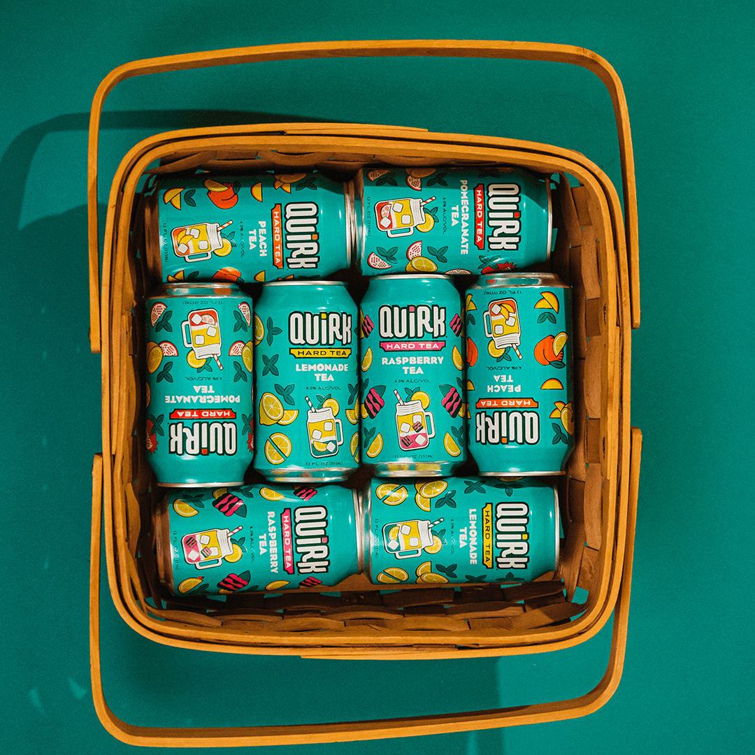 A basket filled with colorful cans of Quirk flavored seltzer, like the "Strawberry Lemonade" and "Peach Tea" from their Tea Mix Pack. The cans are neatly arranged against a teal background, featuring playful fruit illustrations.