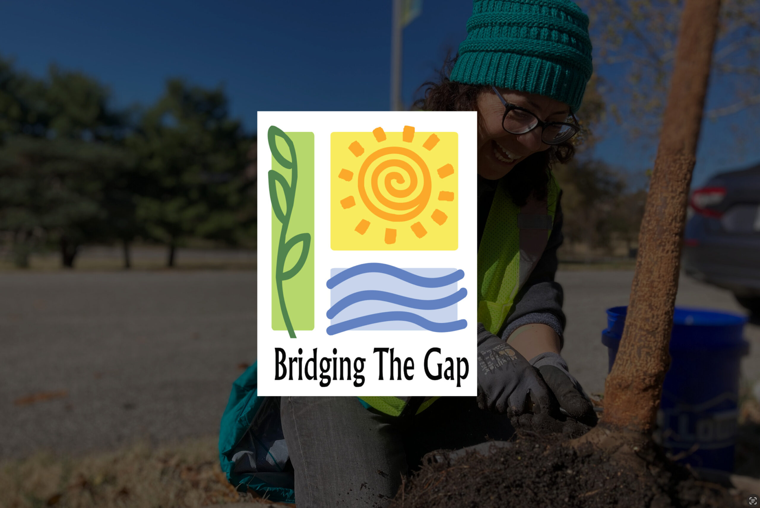 A person wearing glasses and a teal beanie is planting a tree outdoors on a sunny day. The person is smiling and wearing gardening gloves and a yellow vest. Overlaid on the image is a colorful logo with a sun, waves, and plant, reading "Bridging The Gap.