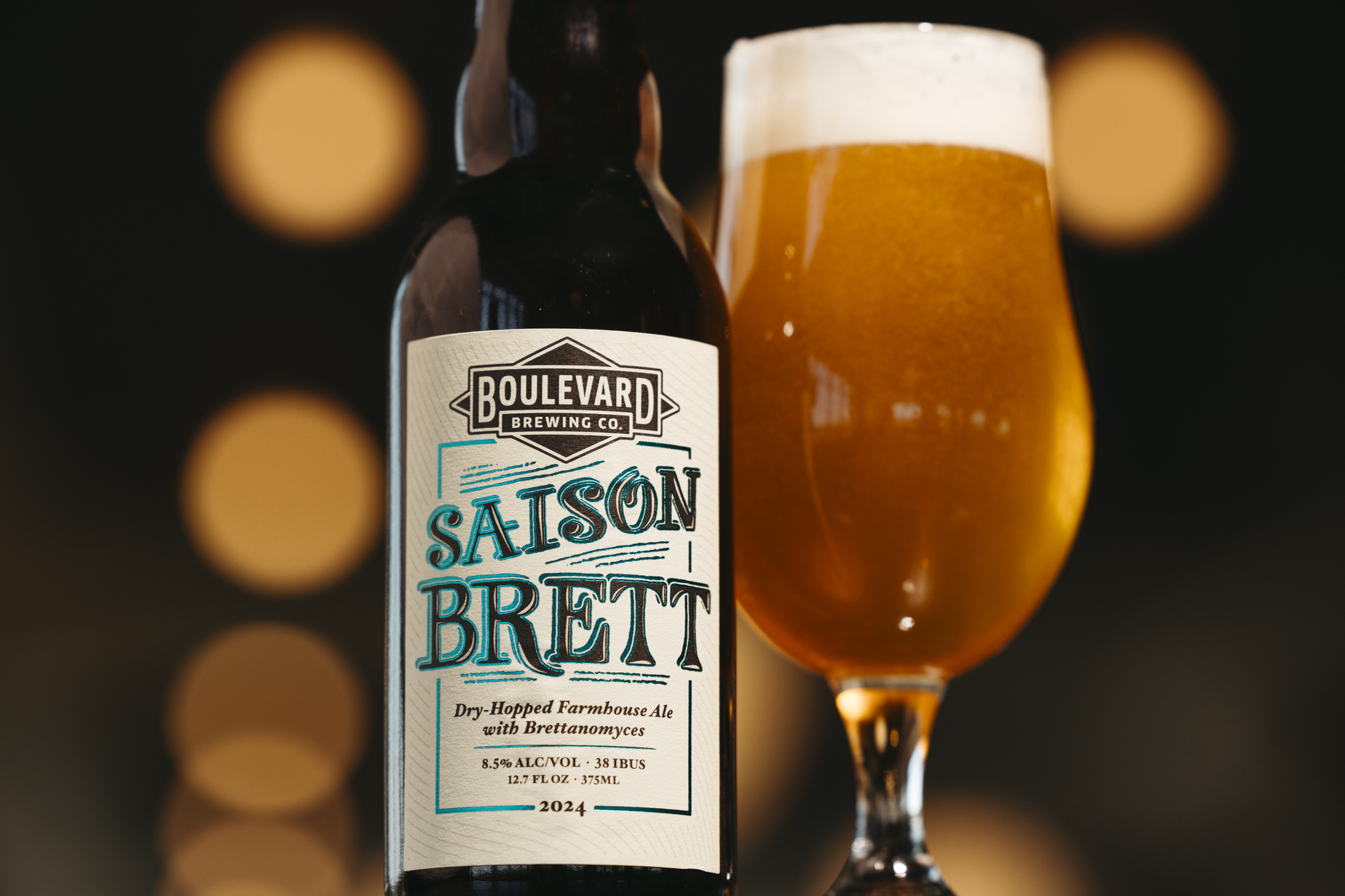 A bottle of Boulevard Brewing Co. Saison Brett beer stands next to a filled glass of frothy golden beer. The label on the bottle highlights its description: "Dry-Hopped Farmhouse Ale with Brettanomyces," with an alcohol content of 8.5% and release date of 2024.